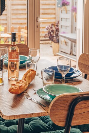 A dining table set with plates, glasses, a bottle, and a baguette. - Apartment Le nid D'Azur by Sur la mer (Mandelieu-la-Napoule)