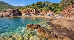 A beach with clear water, rocky formations, and umbrellas. - Apartment Le nid D'Azur by Sur la mer (Mandelieu-la-Napoule)