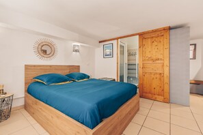 A bedroom with a wooden bed, a small bedside table, a wall clock, and a sliding door. - Apartment Le nid D'Azur by Sur la mer (Mandelieu-la-Napoule)