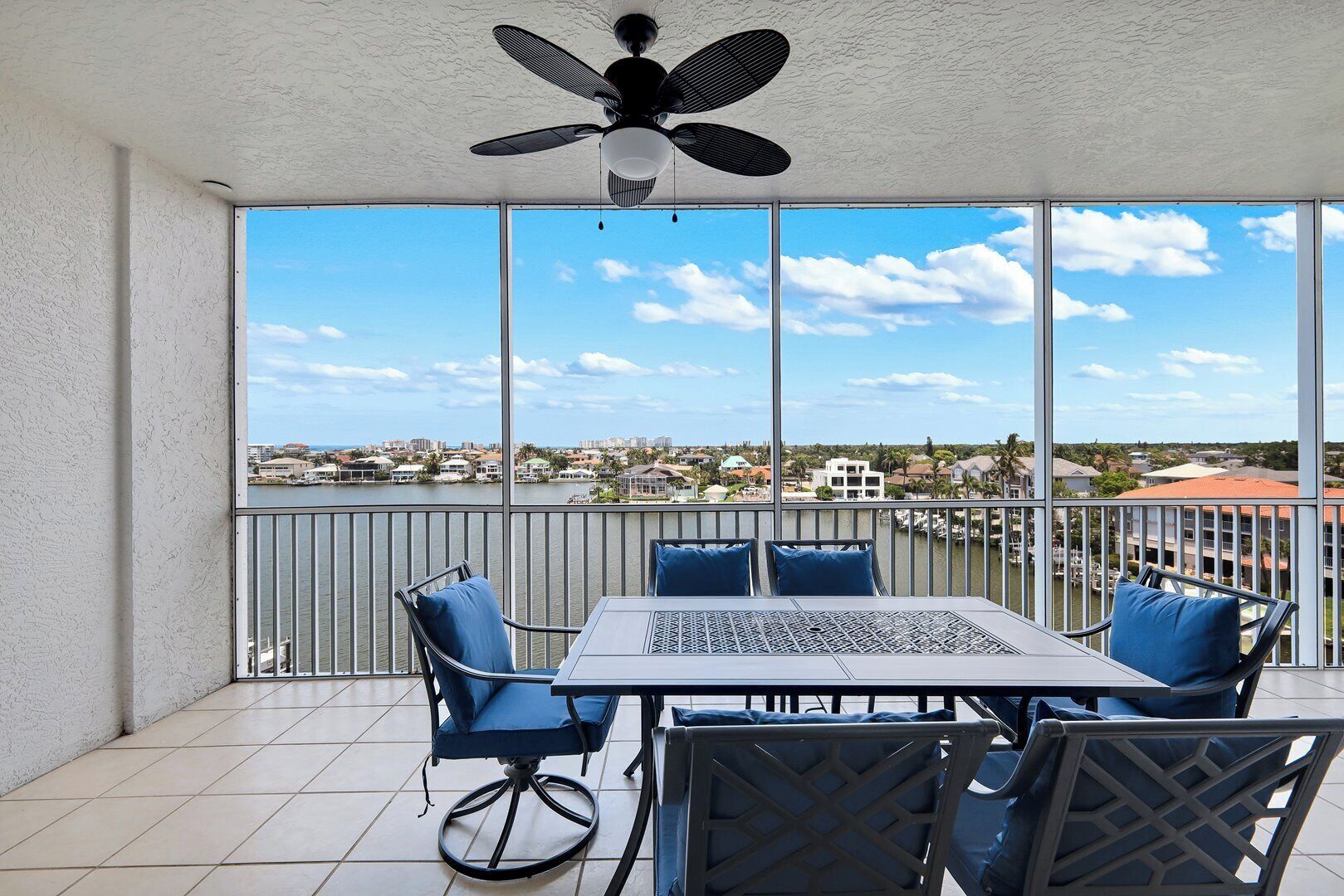A balcony with a table and chairs, a ceiling fan, and a view of a marina and buildings.