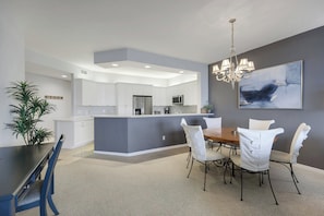 A modern kitchen with white cabinets, a central island, and a dining area with a chandelier. - Regatta - Walk to the Beach! (Naples)