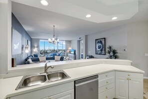 A modern kitchen with a large island, built-in dishwasher, and a view to the living area. - Regatta - Walk to the Beach! (Naples)