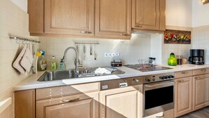A modern kitchen with wooden cabinets, a stainless steel sink, a stove, and a coffee maker. - Holiday Apartment Elisabeth at Lake Plön (Ascheberg (Holstein))