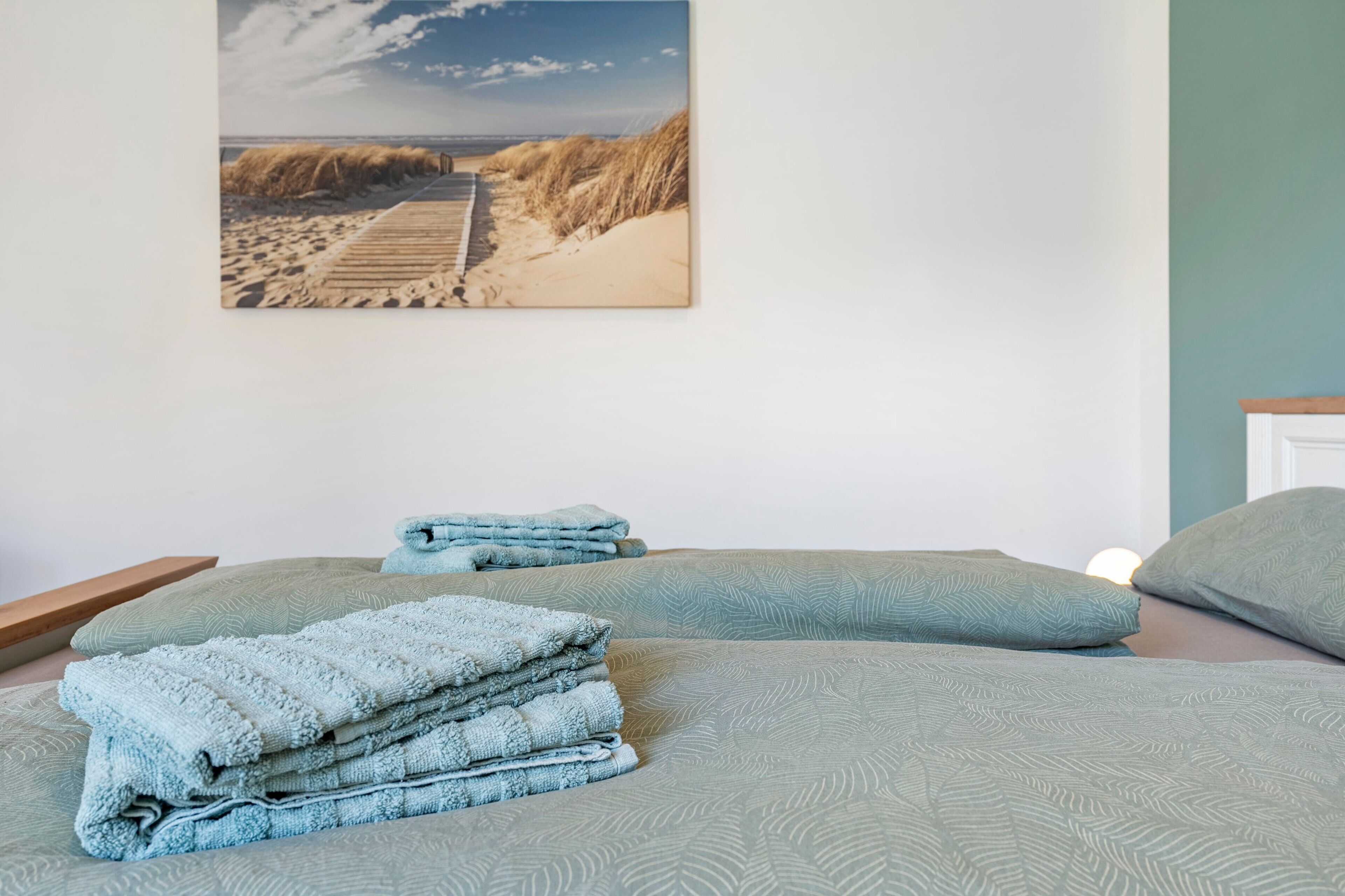 A bedroom with a bed, pillows, and a beach-themed wall art.
