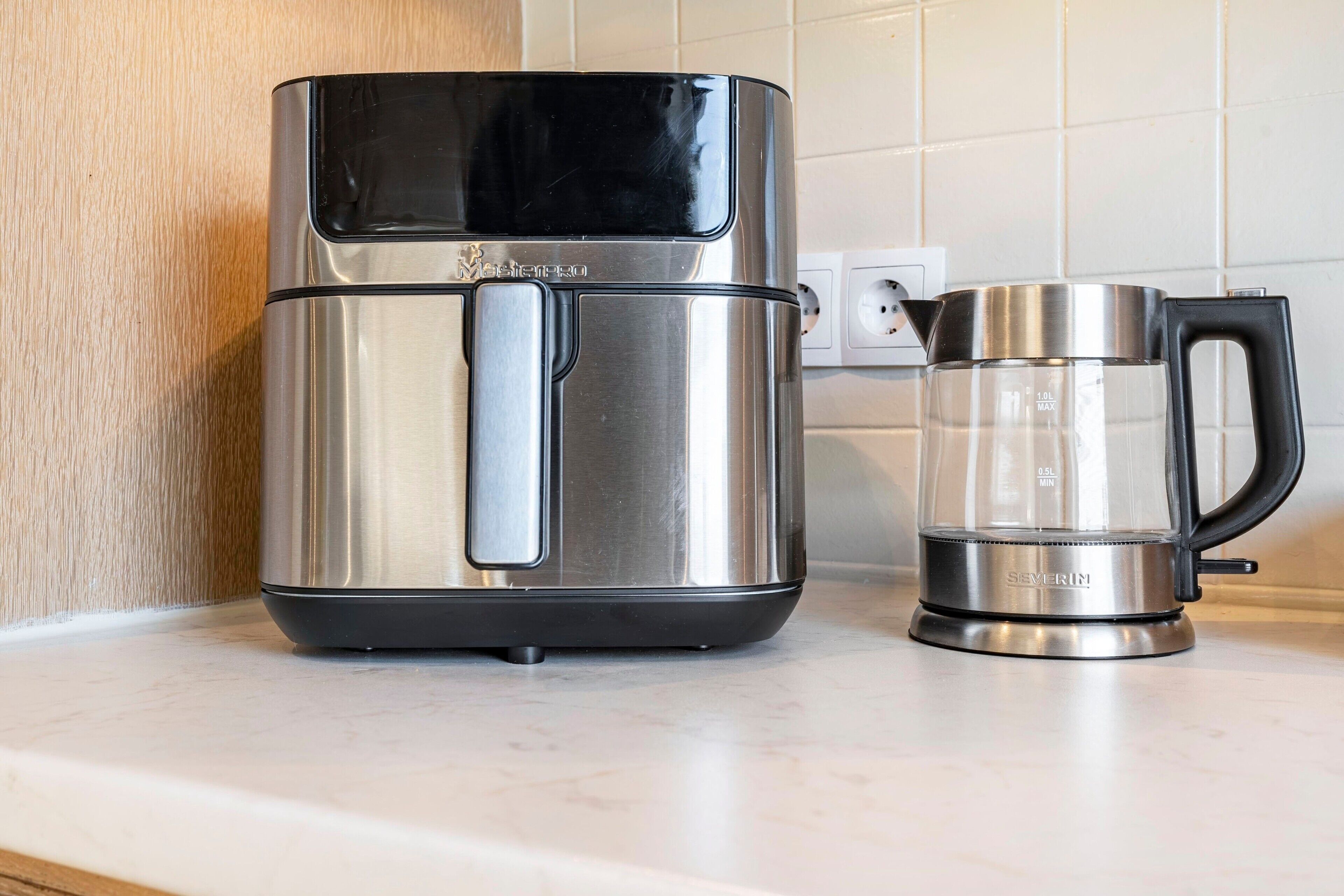 Une cafetière en acier inoxydable dotée d’un couvercle noir et d’une verseuse en verre transparent avec des graduations de mesure, posée sur un plan de travail de cuisine.