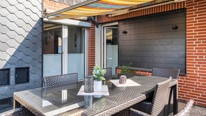 An outdoor patio with a glass table, wicker chairs, and a colorful awning. - Holiday Apartment Elisabeth at Lake Plön (Ascheberg (Holstein))