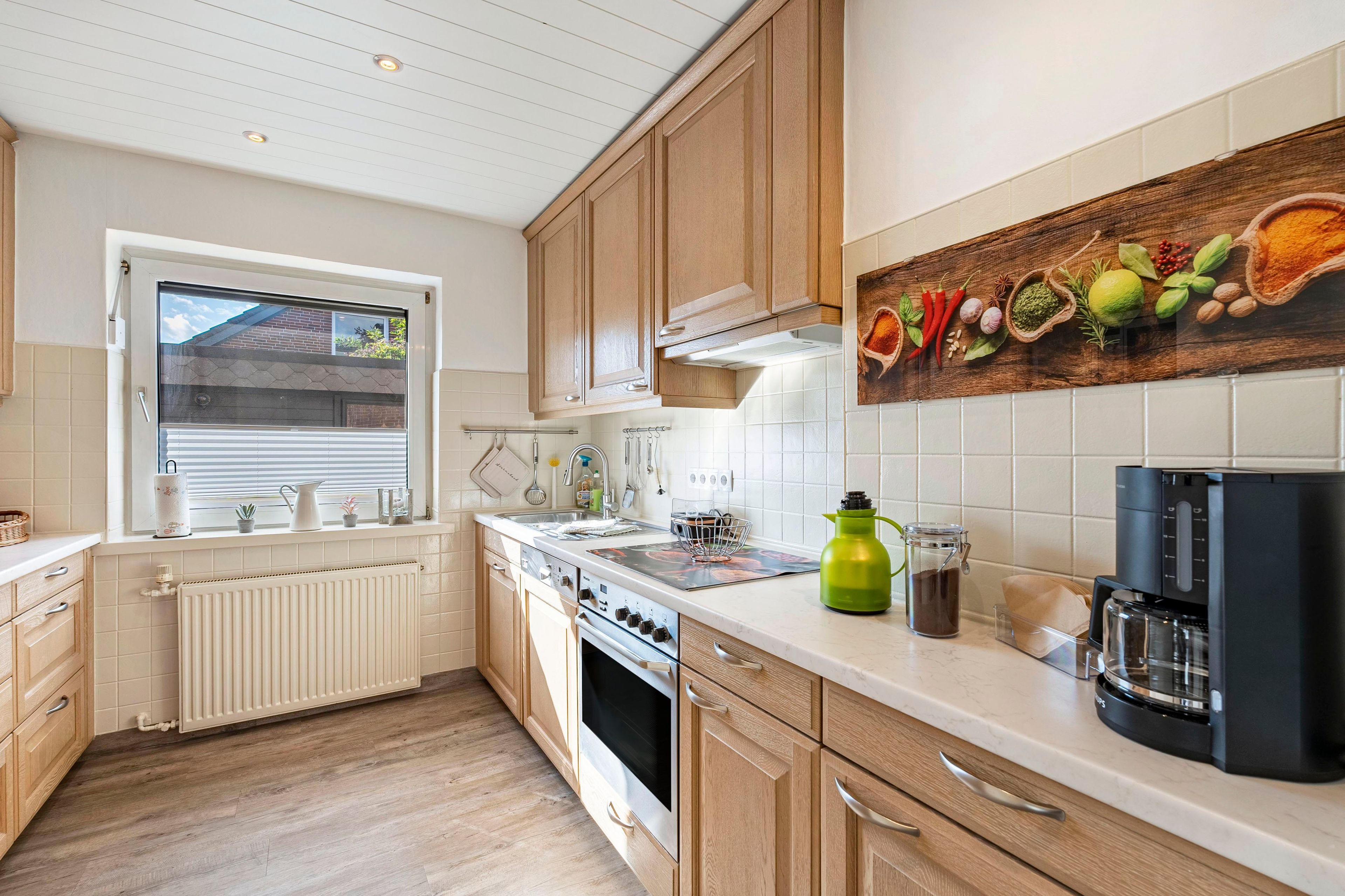 Una cocina moderna con armarios de madera, estufa, pileta y ventana con persianas.