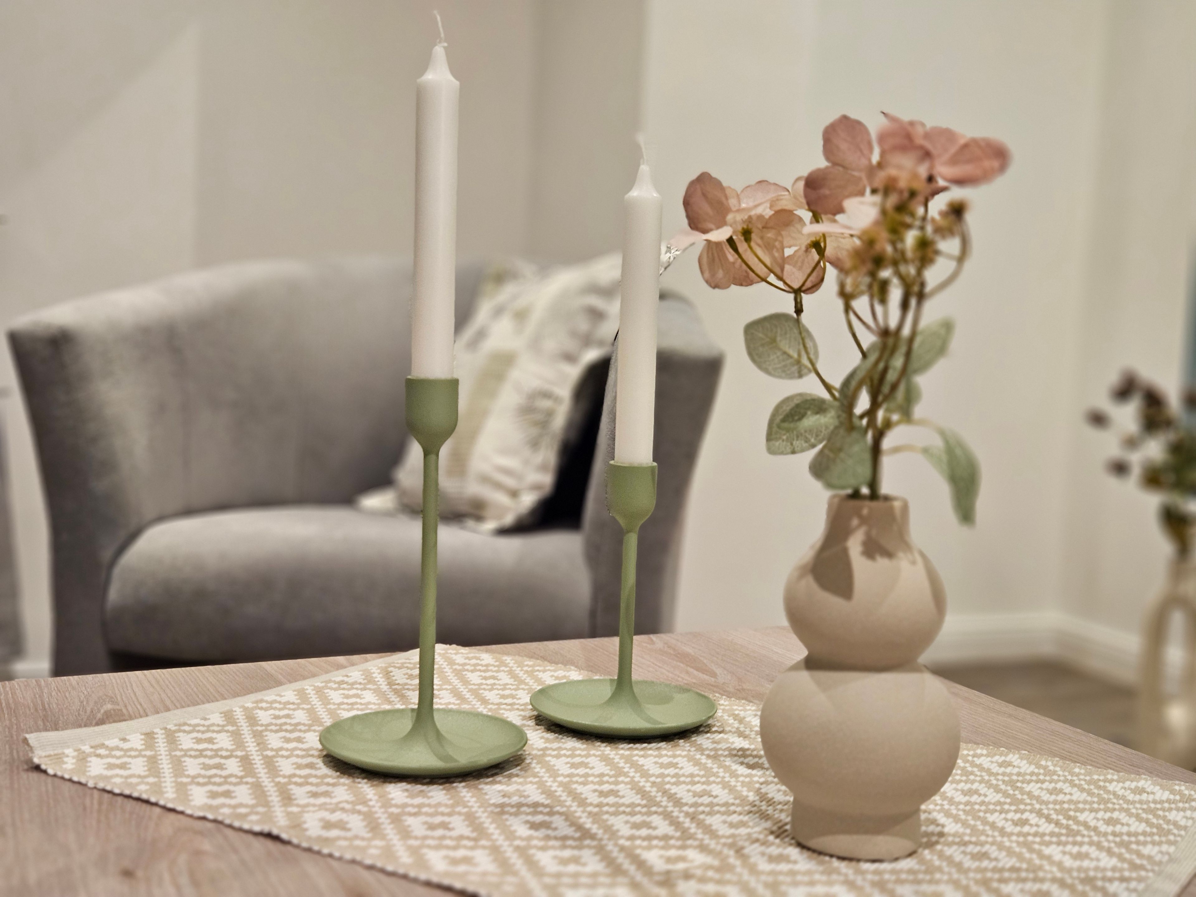A table with two green candle holders and a vase with flowers.