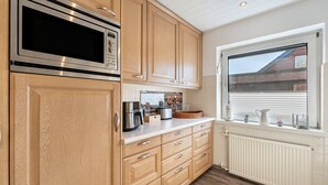 A kitchen with wooden cabinets, a stainless steel microwave, a coffee maker, and a window with a view of a house. - Holiday Apartment Elisabeth at Lake Plön (Ascheberg (Holstein))
