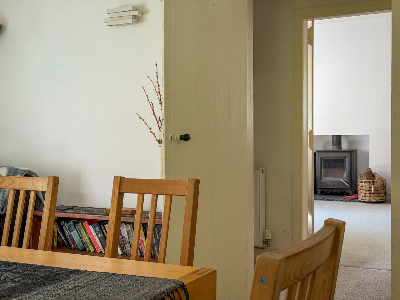 A room with a wooden table, chairs, a bookshelf, a door leading to another room, and a visible fireplace.