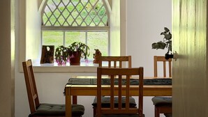 Ein Essbereich mit Tisch, Stühlen, einem Fenster mit Gitterwerk und einer Pflanze auf der Fensterbank.