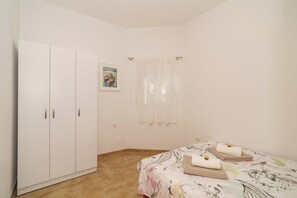 Ein Schlafzimmer mit Bett, Kleiderschrank, einem Fenster mit Vorhängen und einem Bild an der Wand.