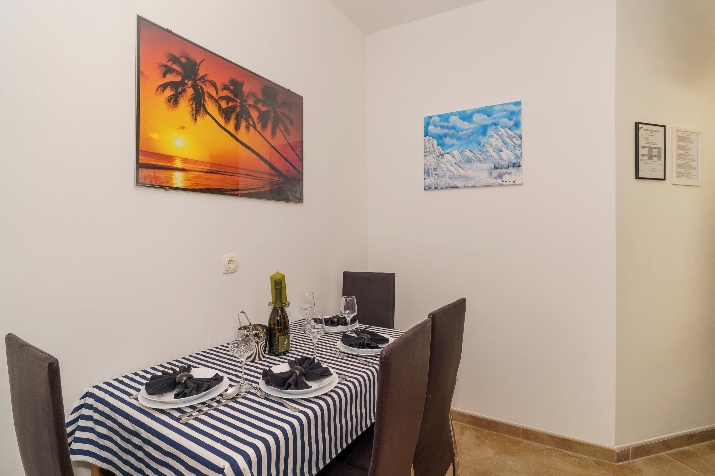 Zona pranzo con tovaglia a righe, una bottiglia di vino e due quadri appesi al muro.