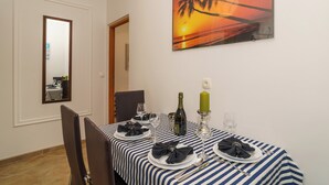 A dining table set with plates, glasses, and a bottle, a painting of a sunset, and a mirror on the wall. - Apartment for 4 people in Dramalj with sea view & parking space (Dramalj)