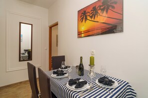 Ein Esstisch ist gedeckt mit Tellern, Gläsern und einer Flasche, ein Sonnenuntergangsbild hängt an der Wand und es befindet sich ein Spiegel dort.
