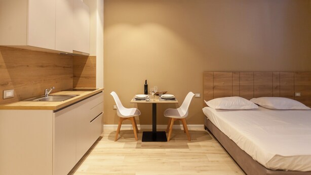 A compact room with a kitchenette, a dining table with chairs, and a bed. - Bus  The Station Apartments (Durrës)