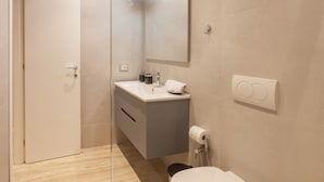 A modern bathroom with a toilet, sink, mirror, and shower. - Bus  The Station Apartments (Durrës)