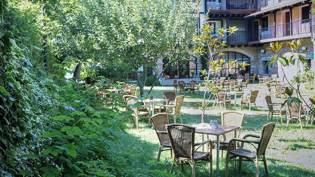 An outdoor patio with wicker furniture and a view of a building with balconies. - Antiguas Eras Hotel (La Alberca)