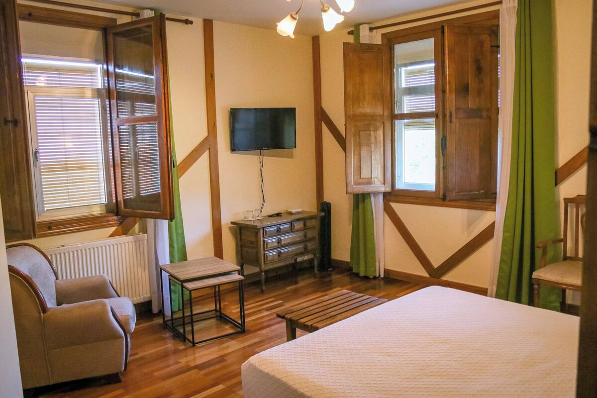 Habitación de hotel con cama, televisión, cómoda, silla y ventana con persianas.