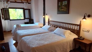 A room with two beds, wooden floors, a painting on the wall, and a window with curtains. - Antiguas Eras Hotel (La Alberca)