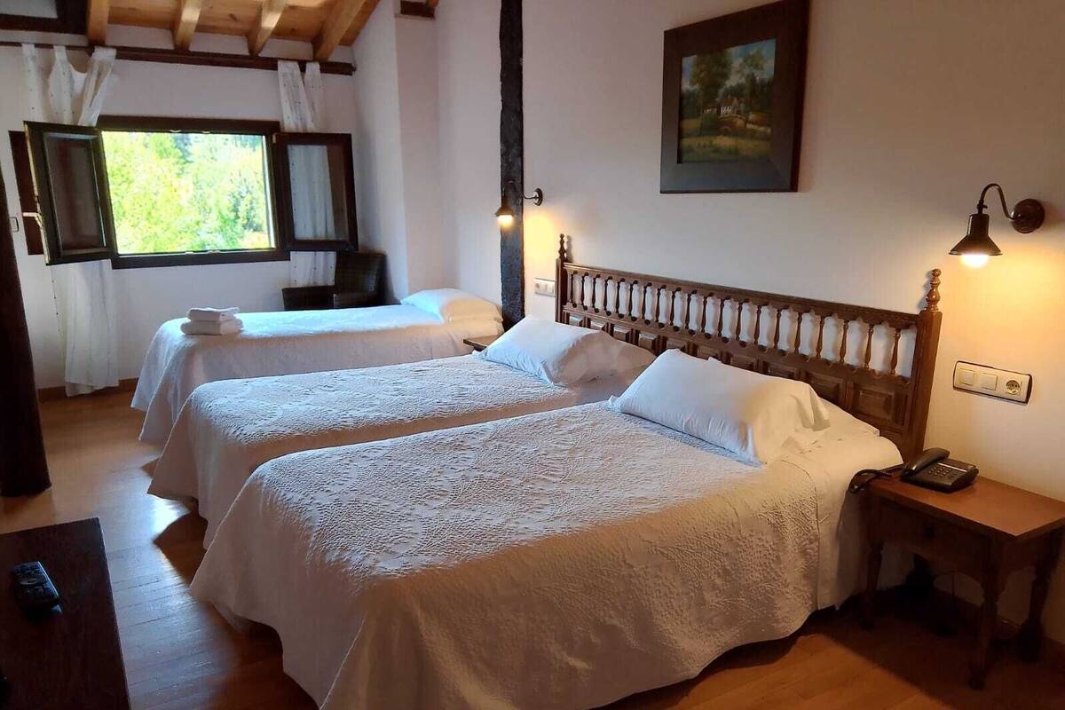 Una habitación con dos camas, piso de madera, un cuadro en la pared y una ventana con cortinas.