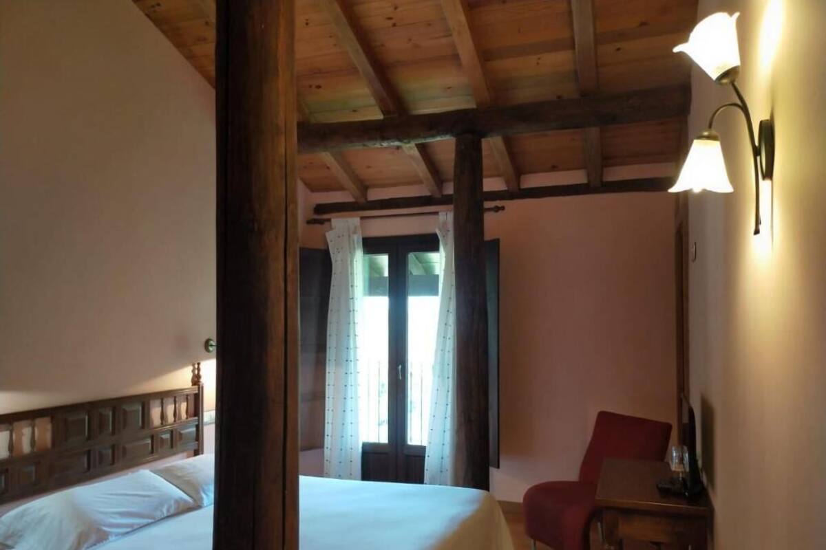 Un dormitorio con cama, una silla, un escritorio y una ventana con cortinas.