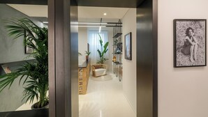 A hallway with a potted plant, a wicker chair, a framed picture on the wall, and a staircase in the background. - Daplace - LE SUITES DEGLI ALTOVITI (Rome)