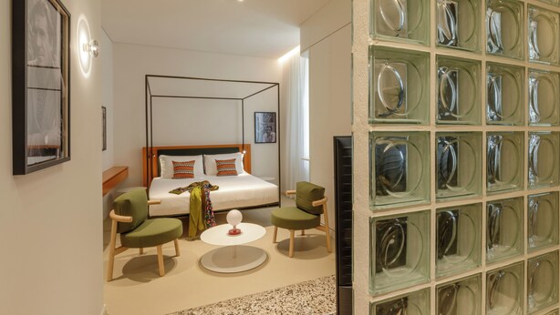 Habitación de hotel moderna con una cama, dos sillas, una mesita y una pared decorada con cristalería.