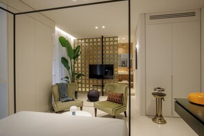 A modern hotel room with a bed, two armchairs, a small table, a television, a decorative plant, and a small table with a lamp. - Daplace - LE SUITES DEGLI ALTOVITI (Rome)