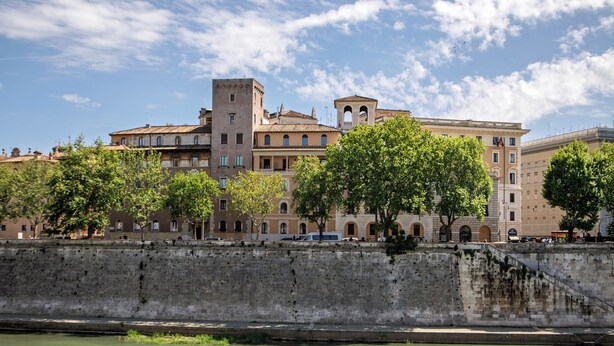 A historic building with multiple stories, a prominent tower, and a river in the foreground. - Daplace - LE SUITES DEGLI ALTOVITI (Rome)
