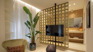 A living room with a TV, a potted plant, a sofa, and a decorative wall panel. - Daplace - LE SUITES DEGLI ALTOVITI (Rome)