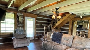 Ein Holzblockhaus-Interieur mit einer Holztreppe, einem Sofa, einem Sessel und einem Deckenventilator.
