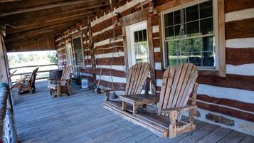A log cabin with a porch, wooden chairs, and a swing.