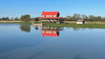 A large house with a red roof, a dock extending into a calm lake, and a small shed nearby.