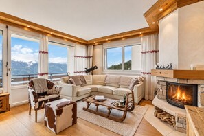 Un salon chaleureux avec une cheminée, une grande fenêtre donnant sur les montagnes et un coin salon confortable.