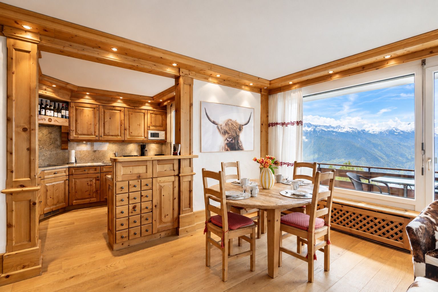 Un intérieur en bois comprenant un coin repas, une cuisine et une grande fenêtre donnant sur les montagnes.