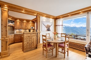Un intérieur en bois comprenant un coin repas, une cuisine et une grande fenêtre donnant sur les montagnes.