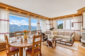 A spacious living area with a wooden dining table, a sofa, and a fireplace. - Nestled in the heart of the Swiss Alps, Peakline Panorama by Mrs Miggins offers an exceptional mount (Crans-Montana)