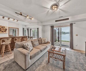 Ein geräumiges Wohnzimmer mit einer Couch, Sesseln, einem Couchtisch und Blick auf einen See durch große Fenster.