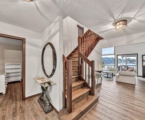 Ein großzügiger Wohnbereich mit einer Holztreppe, einem großen Spiegel und Blick ins Freie.