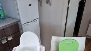 Eine Küchenzeile mit einem weißen Kühlschrank, einem Holzschrank und einem weißen Stuhl mit grüner Sitzfläche.