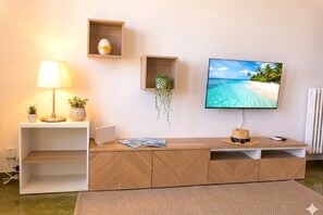 Ein modernes Wohnzimmer mit Fernseher, Lampe, einer kleinen Pflanze und einem Regal mit Dekoration.