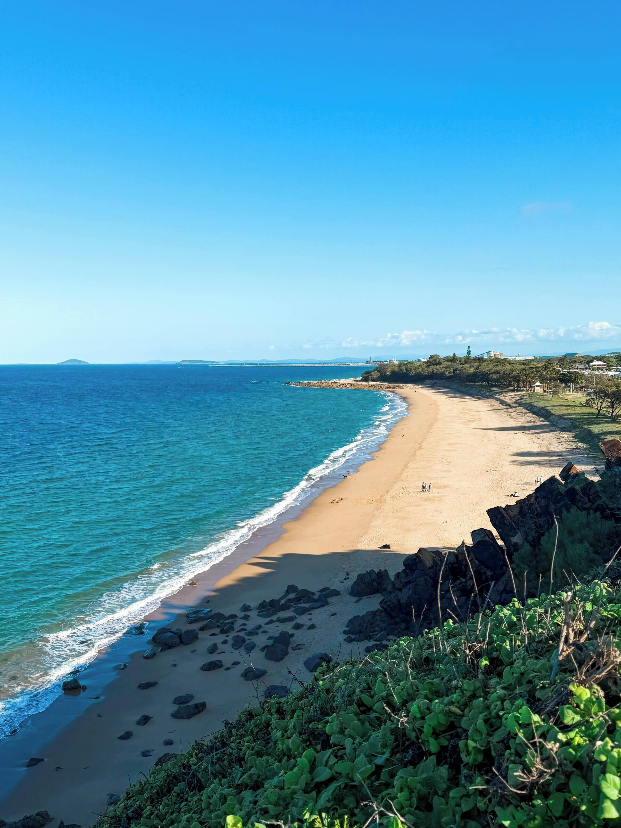 A beach with clear blue water, sandy shore, and rocky outcrops.