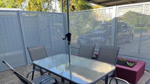 En udendørs terrasse med et glasbord og fire stole, omgivet af et jerngærde.
