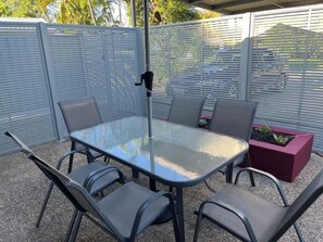 An outdoor patio with a glass-top table and four chairs, surrounded by a metal fence. - Lambert's Beach Awaits with Wifi (Slade Point)