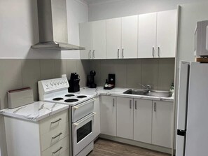 Een moderne keuken met witte kastjes, een inbouwfornuis, een spoelbak en een koffiezetapparaat.