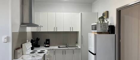 A compact kitchen with white cabinets, a stove, a sink, and a microwave.