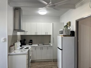 Cocina compacta con armarios blancos, estufa, pileta y microondas.
