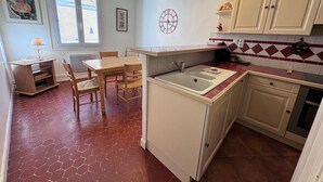 A compact kitchen with a dining area, a sink, and a window with blinds. - La Maison Barillerie 4 - Old Town (Nice)