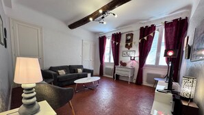 A living room with a sofa, a coffee table, a lamp, a side table, a clock, and a window with curtains. - La Maison Barillerie 4 - Old Town (Nice)